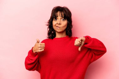 Pembe arka planda izole edilmiş genç İspanyol kadın baş parmağını kaldırıyor, zor seçim konsepti.