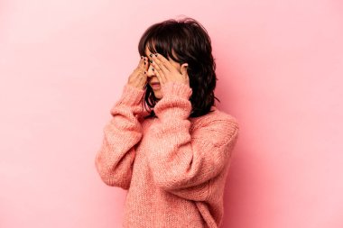 Pembe arka planda izole edilmiş genç İspanyol kadın elleriyle gözlerini kapatmaktan korkuyor..