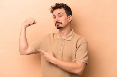 Beyaz tenli genç adam bej arka planda izole edilmiş. Güçlü bir hareket sergiliyor. Kadın gücünün sembolü.