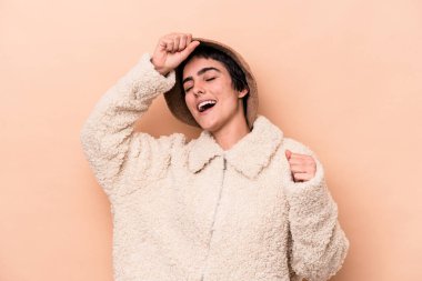 Beyaz tenli genç bir kadın, bej arka planda izole edilmiş özel bir günü kutluyor, atlıyor ve enerji ile kollarını kaldırıyor..