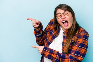 Mavi arka planda izole edilmiş beyaz, genç bir kadın işaret parmağıyla işaret ederek heyecanlanıyor..