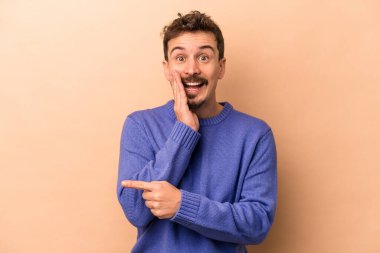 Beyaz tenli genç adam bej arka planda izole edilmiş. Dedikodu yapıyor, bir şeyleri bildiriyor..