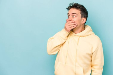 Kafkasyalı genç adam mavi arka planda izole edilmiş. Düşünceli bir şekilde ağzıyla ağzını kapatan bir fotokopi odasına bakıyor..