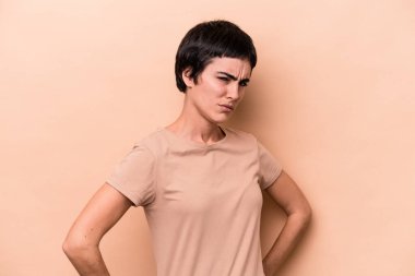 Young caucasian woman isolated on beige background frowning face in displeasure, keeps arms folded. clipart