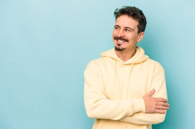 Mavi arka planda izole edilmiş genç beyaz adam kollarını kavuşturarak gülümsüyor..