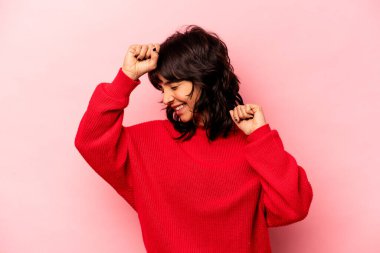 Pembe arka planda izole edilmiş genç İspanyol kadın özel bir günü kutluyor, atlıyor ve enerjiyle kollarını kaldırıyor..