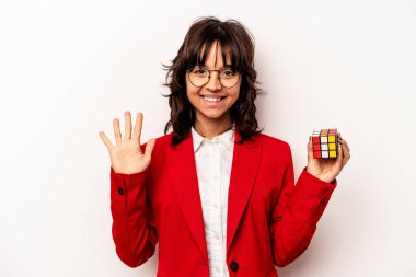 Beyaz arka planda Rubiks küpünü tutan genç bir iş kadını gülümseyerek beş numarayı parmaklarıyla gösteriyor.