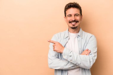 Beyazların arka planında izole edilmiş genç beyaz adam işaret parmağıyla işaret ederek gülümsüyor..