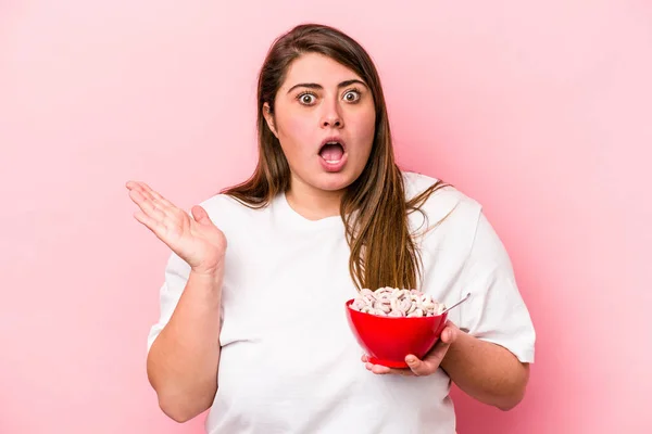 年轻的高加索超重女人拿着一碗谷类食物 从粉红的背景中分离出来 感到惊讶和震惊 — 图库照片