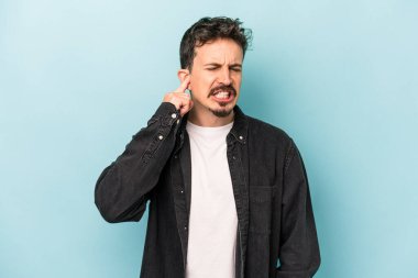 Genç beyaz adam mavi arka planda izole edilmiş parmaklarıyla kulaklarını kapatıyor, gürültülü bir ortam tarafından stresli ve umutsuz..
