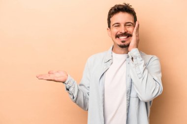 Beyazların arka planında izole edilmiş genç beyaz bir adam bir avuç içinde fotokopi alanı tutuyor, el üstünde tutuyor. Şaşırmış ve mutlu..