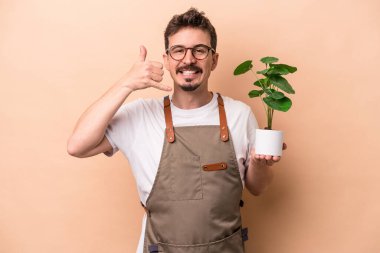 Beyaz tenli genç bahçıvan elinde bej arka planda izole edilmiş bir bitki tutuyor. Cep telefonu hareketini parmaklarıyla gösteriyor..