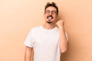 Beyazlı genç adam bej arka planda izole edilmiş zafer, tutku ve coşkuyu kutluyor, mutlu bir ifade..