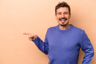 Beyazların arka planında izole edilmiş genç beyaz adam işaret parmağıyla işaret ederek gülümsüyor..