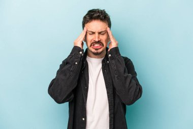 Genç beyaz adam mavi arka planda izole edilmiş tapınaklara dokunuyor ve başı ağrıyor..