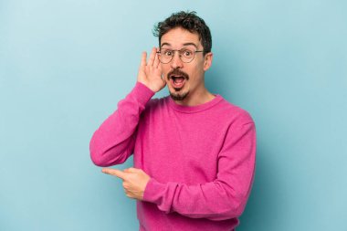 Mavi arka planda izole edilmiş genç beyaz adam bir dedikoduyu dinlemeye çalışıyor..