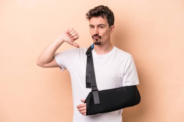 Kırık kollu genç beyaz adam bej arka planda izole edilmiş gururlu ve kendinden emin, örnek olarak.