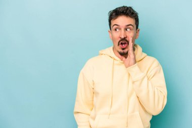 Mavi arka planda izole edilmiş genç beyaz bir adam gizli bir sıcak fren haberi veriyor ve yana bakıyor.