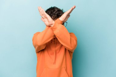 Kafkasyalı genç adam mavi arka planda izole edilmiş iki kolu çapraz tutuyor, inkar kavramı.