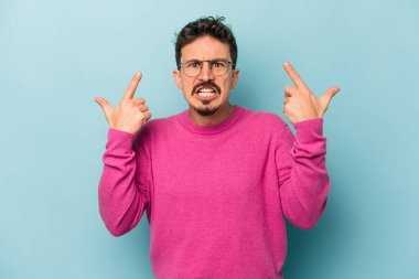 Mavi arka planda izole edilmiş genç beyaz adam işaret parmağıyla bir hayal kırıklığı jesti gösteriyor..
