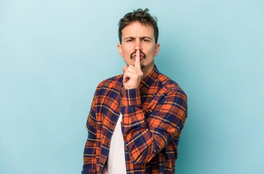 Mavi arka planda izole edilmiş genç beyaz bir adam ya sır saklıyor ya da sessizlik istiyor..