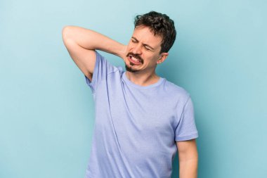 Kafkasyalı genç adam mavi arka planda izole edilmiş. Yorgun ve uykulu. Elini başının üstünde tutuyor..