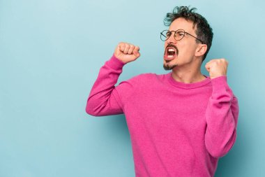 Mavi arka planda izole edilmiş genç beyaz bir adam zaferden sonra yumruğunu kaldırıyor, kazanan konsept..