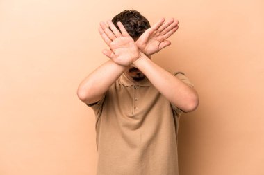 Beyazlı genç adam bej arka planda izole edilmiş iki kolu çapraz tutuyor, inkar kavramı.