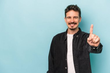 Mavi arka planda izole edilmiş genç beyaz adam bir numarayı parmağıyla gösteriyor..