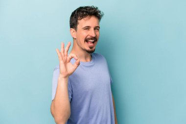 Kafkasyalı genç adam mavi arka planda izole edilmiş neşeli ve kendinden emin..