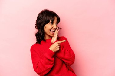 Genç İspanyol kadın pembe arka planda izole edilmiş. Dedikodu yapıyor, bir şeyleri bildiriyor..