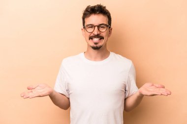 Beyazlı genç bir adam bej arka planda izole edilmiş, kollarıyla ölçek yapıyor, mutlu ve kendinden emin hissediyor..