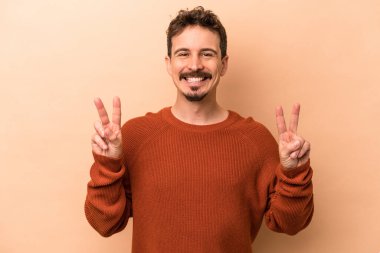 Beyazların arka planında izole edilmiş genç beyaz adam zafer işareti gösteriyor ve gülümsüyor..