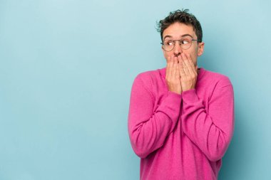 Kafkasyalı genç adam mavi arka planda izole edilmiş. Düşünceli bir şekilde ağzıyla ağzını kapatan bir fotokopi odasına bakıyor..