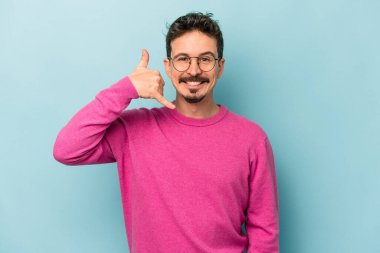 Mavi arka planda izole edilmiş genç beyaz adam parmaklarıyla bir cep telefonu hareketi gösteriyor..