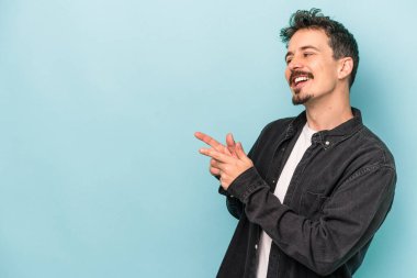 Kafkasyalı genç adam mavi arka plan noktalarında izole edilmiş başparmak uzakta, gülüyor ve kaygısız.