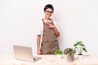 Beyaz arka planda izole edilmiş genç bahçıvan kadın gülümsüyor ve boş alanda bir şey gösteriyor..
