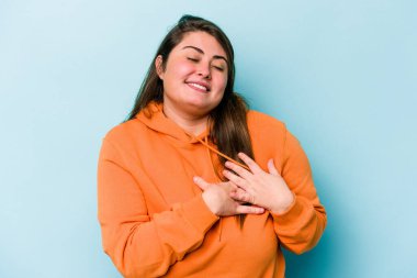 Mavi arka planda izole edilmiş beyaz tenli genç bir kadın, dostane bir ifadeye sahip, avuçlarını göğsüne bastırıyor. Aşk konsepti.