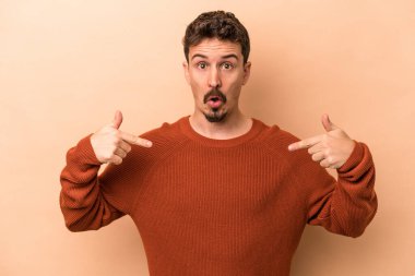 Beyazlı genç bir adam bej arka planda izole edilmiş. Parmakları aşağıda, olumlu hisler içinde..