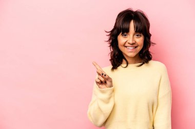 Pembe arka planda izole edilmiş genç İspanyol kadın işaret parmağıyla işaret ederek gülümsüyor..