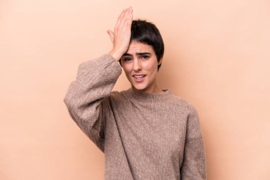 Beyaz tenli genç bir kadın bej arka planda izole edilmiş bir şekilde bir şey unutuyor. Alnına avuç içi ve kapalı gözlerle vuruyor..