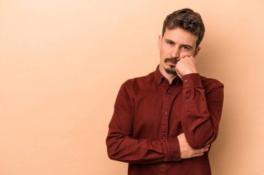 Bej arka planda izole edilmiş, üzgün ve dalgın hisseden, fotokopi alanına bakan genç beyaz bir adam..