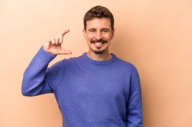 Beyaz tenli genç adam bej arka planda izole edilmiş. Elinde parmakları olan, gülümseyen ve kendinden emin bir şey var..