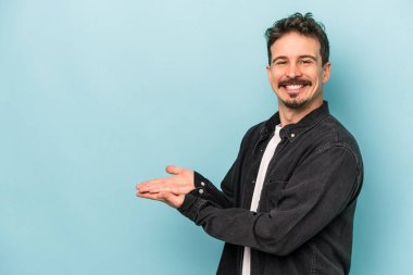 Mavi arka planda izole edilmiş genç beyaz bir adam palmiyesinde bir kopya alanı tutuyor..
