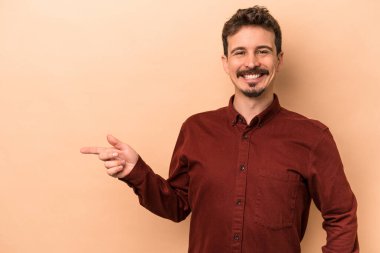 Beyazların arka planında izole edilmiş genç beyaz adam işaret parmağıyla işaret ederek gülümsüyor..
