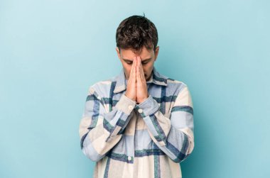 Kafkasyalı genç adam mavi arka planda izole edilmiş dua ediyor, bağlılık gösteriyor, dindar biri ilahi ilham arıyor..