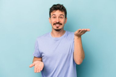 Mavi arka planda izole genç beyaz adam kollarıyla ölçek yapar, mutlu ve kendinden emin hisseder..