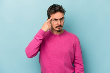 Mavi arka planda izole edilmiş genç beyaz bir adam şakağı parmağıyla işaret ediyor, düşünüyor ve bir göreve odaklanıyor..