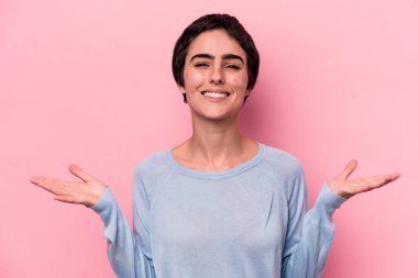 Pembe arka planda izole edilmiş genç beyaz kadın kollarıyla ölçek oluşturuyor, mutlu ve kendinden emin hissediyor..