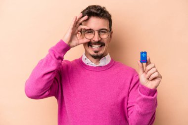 Elinde batarya tutan genç beyaz adam bej arka planda izole edilmiş..